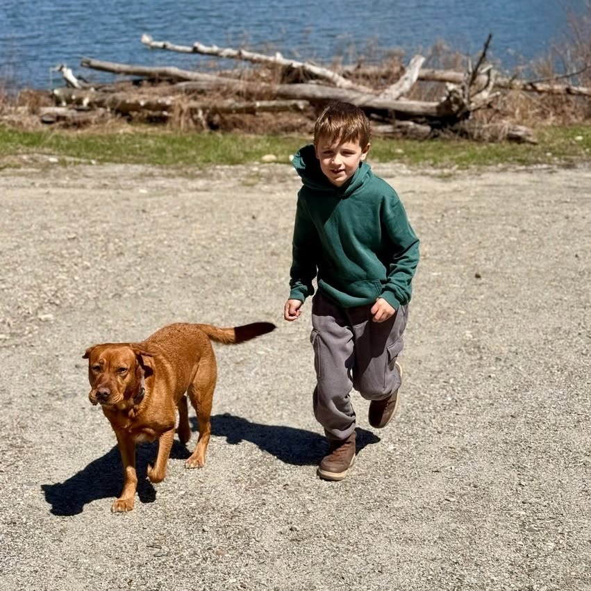 Mason Sundberg and his dog walking on a gravel path near a body of water.