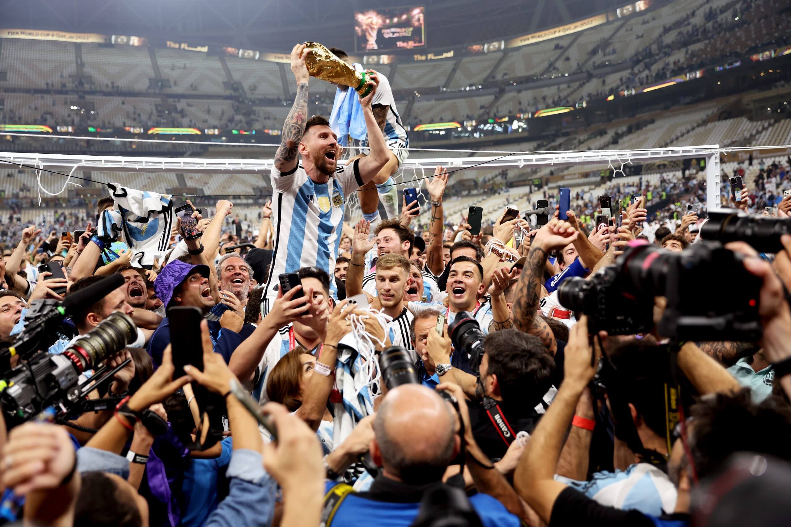 Messi lifting the World Cup trophy while being carried by Argentina team-mates surrounded by players and media