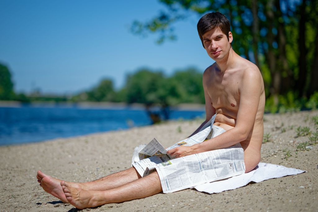 Mannheim City Councillor Julien Ferrat sitting nude on Friesenheim Island with a newspaper, looking towards the camera.