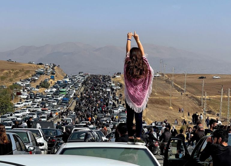 This image posted on Twitter shows an unveiled woman standing on top of a vehicle as thousands make their way towards Aichi cemetery in Saqqez, Mahsa Amini’s hometown in the western Iranian province of Kurdistan, to mark 40 days since her death, defying heightened security measures as part of a bloody crackdown on women-led protests [AFP]