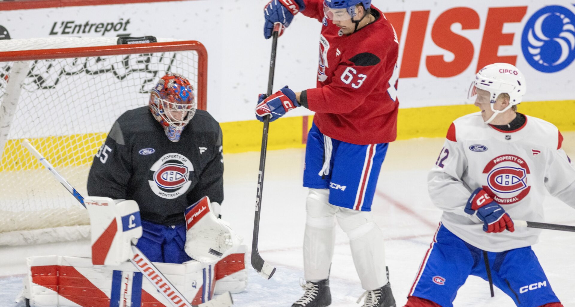 Forward Florian Xhekaj tries to deflect the puck in front of goalie Samuel Montembeault and behind defenceman Adam Engstrom during Montreal Canadiens training camp practice