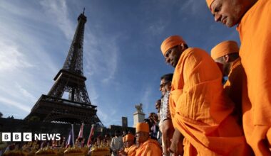 A man wearing a backpack is out of focus in the foreground of the picture, which shows the entrance to the Eiffel Tower and a sign showing that it is closed.