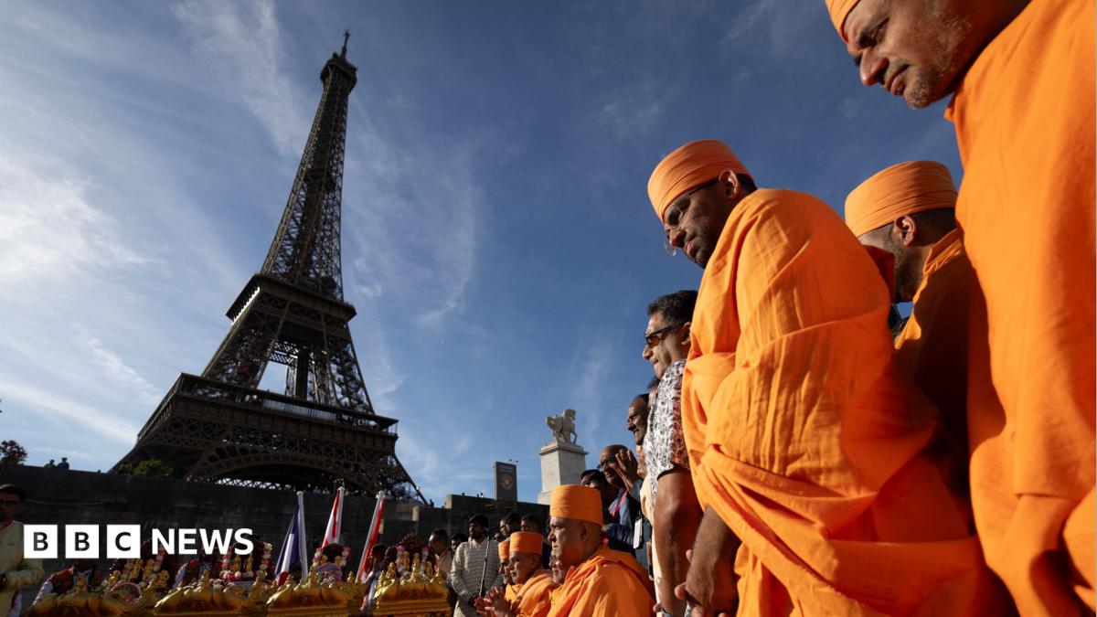 A man wearing a backpack is out of focus in the foreground of the picture, which shows the entrance to the Eiffel Tower and a sign showing that it is closed.