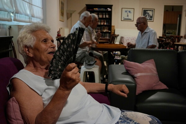 Jenny Sakellariou uses a hand fan while men play backgammon in an air-conditioned cooling center operated by the Athens municipality throughout a heat wave in Athens, Greece, Aug. 24, 2026. (AP Photo/Thanassis Stavrakis, File)