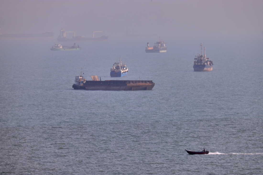 A small boat sails past cargo ships and other commercial vessels anchored in the Strait of Hormuz off Bandar Abbas, Iran, on Aug. 5.