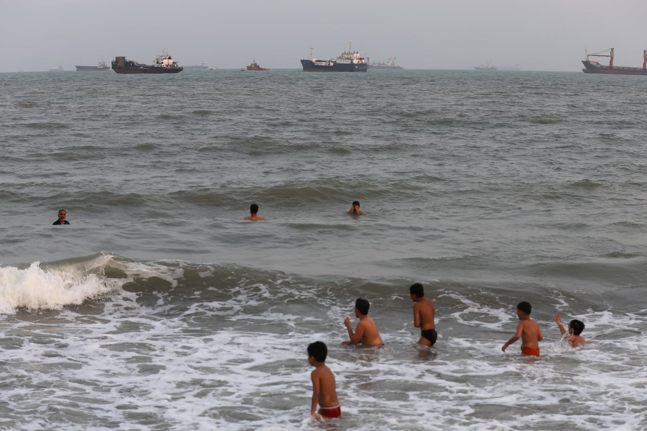 Children swim in the sea as ships are seen in the distance.