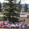 A woman in dark clothes mourns at a makeshift memorial for the victims of a deadly mass shooting that took place at Tumbler Ridge Secondary School, in the town of Tumbler Ridge, British Columbia, Canada. The memorial consists of stuffed animals and flowers at the base of a conifer tree.