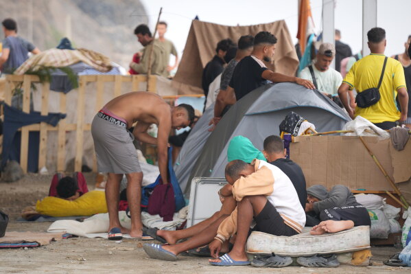 Migrants stand near their tents at El Trampolín beach in the Spanish exclave of Ceuta, Wednesday, Sept. 2, 2026. (AP Photo/Francis González)