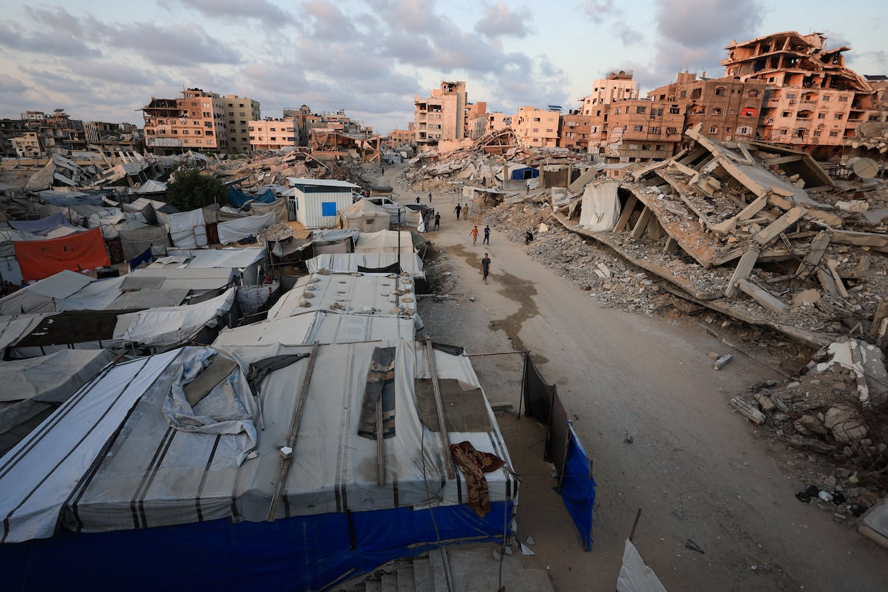 People walk past rubble and damaged buildings.