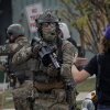 A federal law enforcement agent dressed in camouflage clothing confronts a demonstrator wearing a blue baseball cap with her back to the camera.