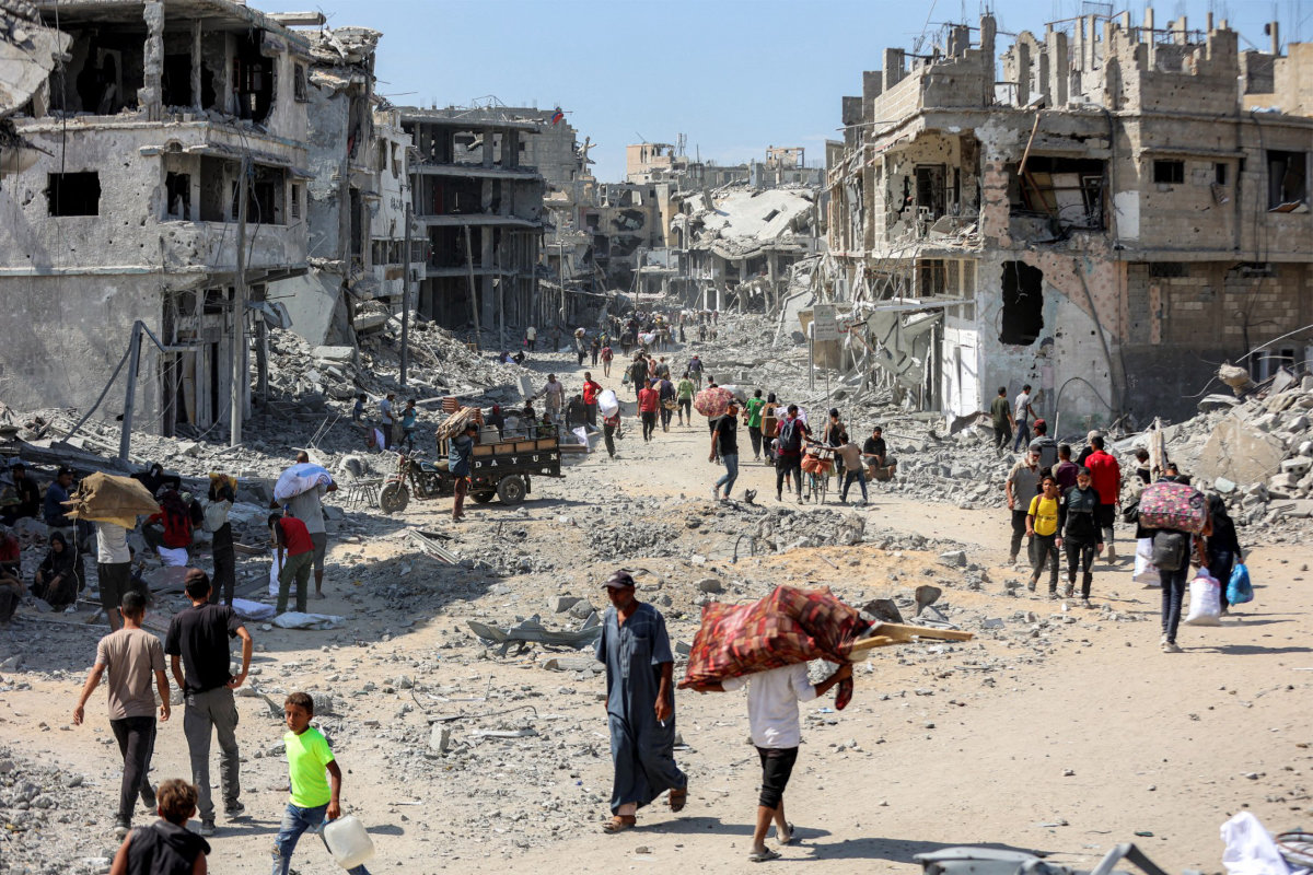 People walk along a destroyed road past heavily-damaged buildings in the centre of Khan Yunis in the southern Gaza Strip on October 10, 2025, as the displaced return to their homes after Israeli forces' withdrawal. (AFP/File)