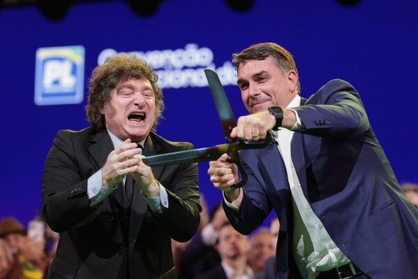 Brazilian Sen. Flavio Bolsonaro, right, handles an oversized pair of scissors, accompanied by Argentina's President Javier Milei during the Liberal Party convention where Bolsonaro was confirmed as the party's presidential candidate, in Sao Paulo, Saturday, July 25, 2026. (AP Photo/Ettore Chiereguini)