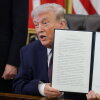 Seated at a desk in the White House's Oval Office in March, President Trump holds up an executive order calling to restrict mail-in voting.