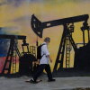 A pedestrian wearing a backpack walks past a mural featuring oil wells.