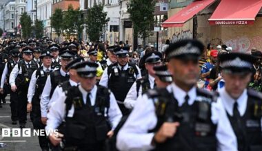 Dozens of members of the Metropolitan Police walk in uniform through the Notting Hill Carnival