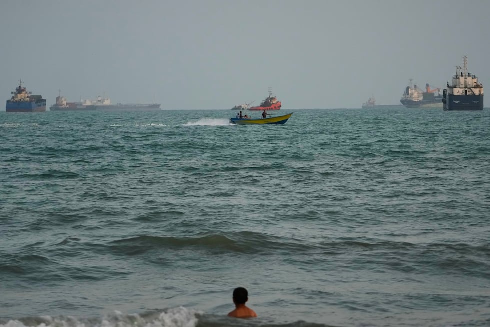 A swimmer remains near the shore as a motorboat passes commercial vessels anchored in the...