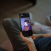 Debbie Willson holds her smartphone, which is displaying a photo of her son, Adam Willson, who died at age 27 in 2024. Adam is wearing a T-shirt that says "Jason Lives," with an image of the horror movie character Jason holding an axe above his head.