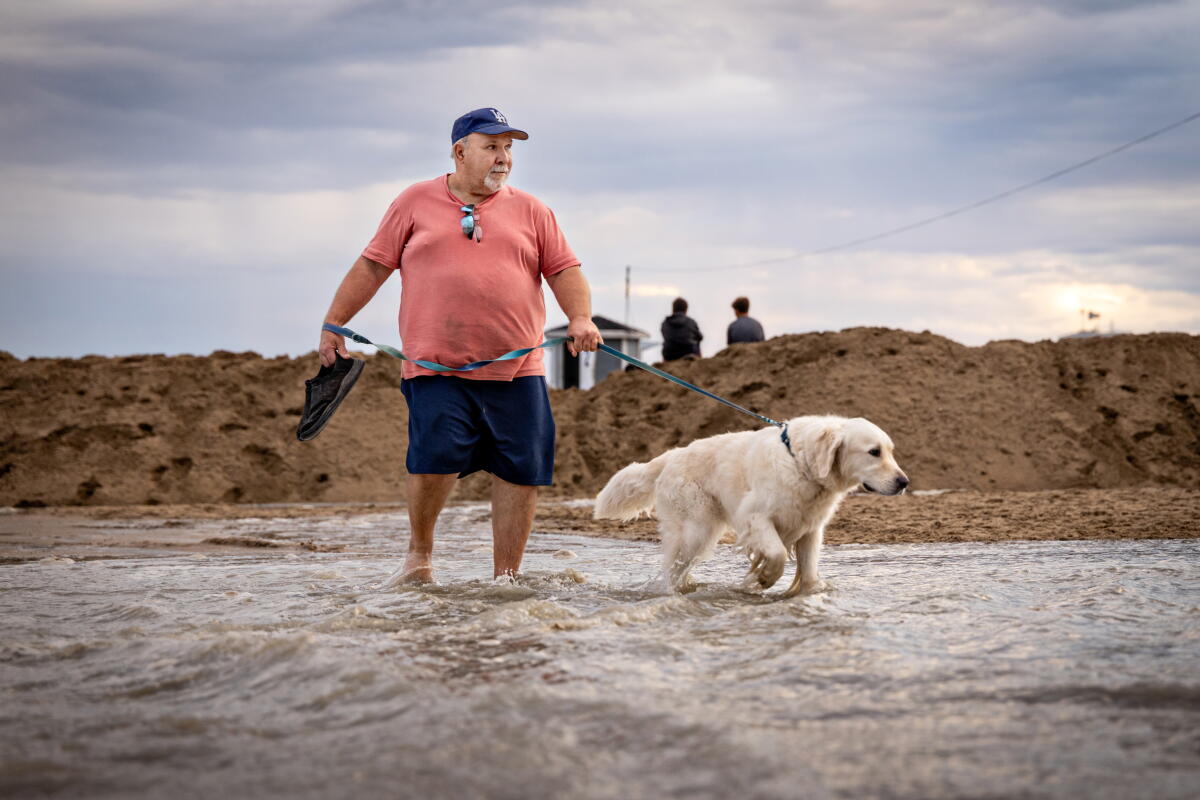 Mark Roslawski and his dog, Benni, walk through a flooded parking lot near the Seal Beach Pier.