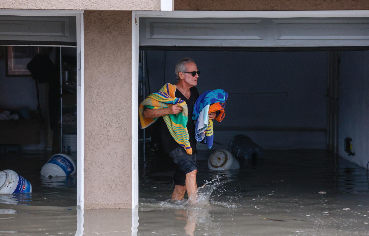 A man carries beach towels out of a flooded garage.