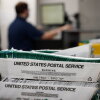 Election workers stack ballots that were picked up at a U.S. Postal Service office. The bin says United States Postal Service on the side.