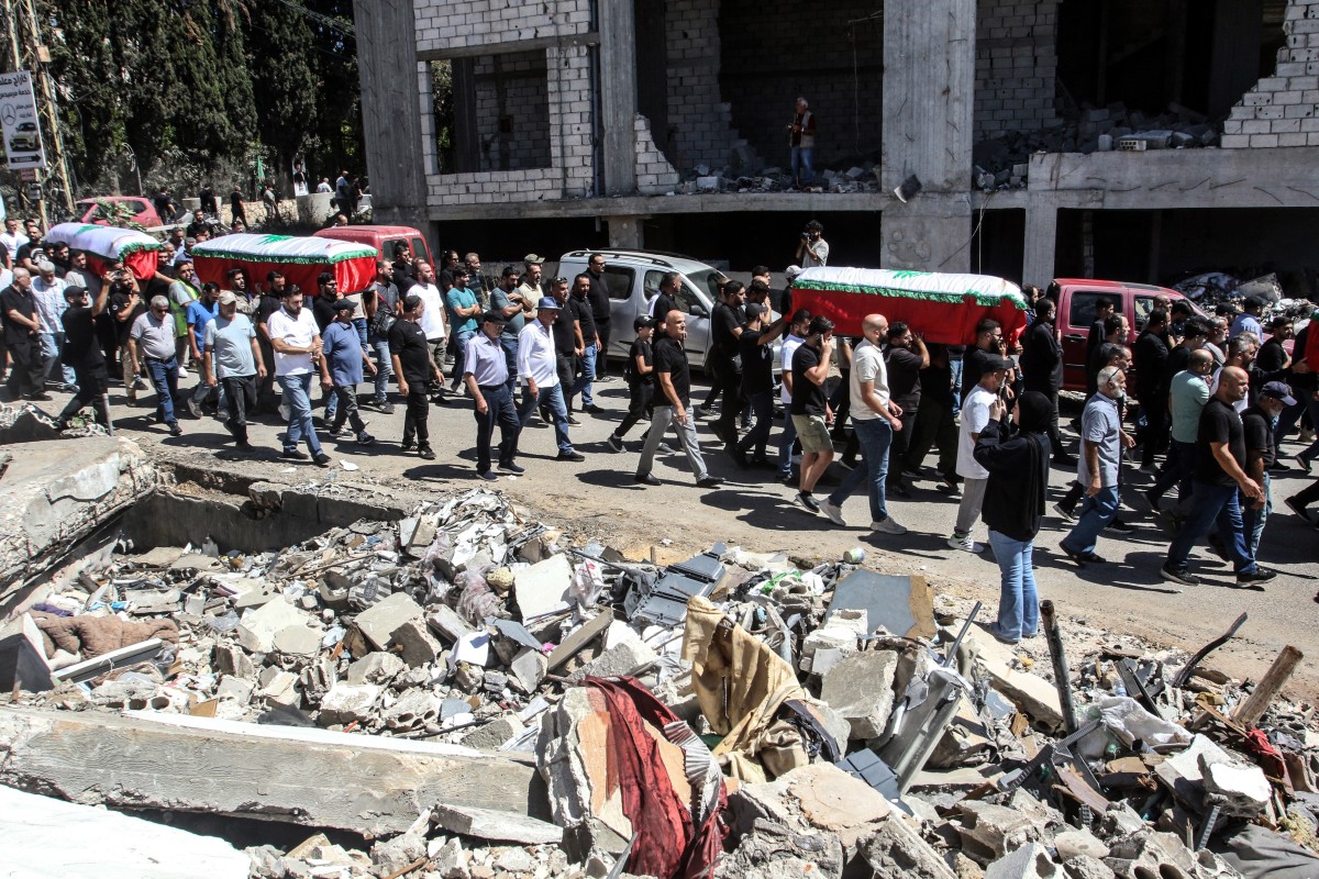 Mourners carry the coffins past the debris of destroyed buildings of Lebanese killed the day before in an Israeli air strike that targeted the southern Lebanese village of Kfar Rumman on Sept. 8, 2026. (AFP)