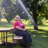 A woman wearing a long skirt and an "America needs unions" T-shirt sits at a picnic table in the shade of a tree.