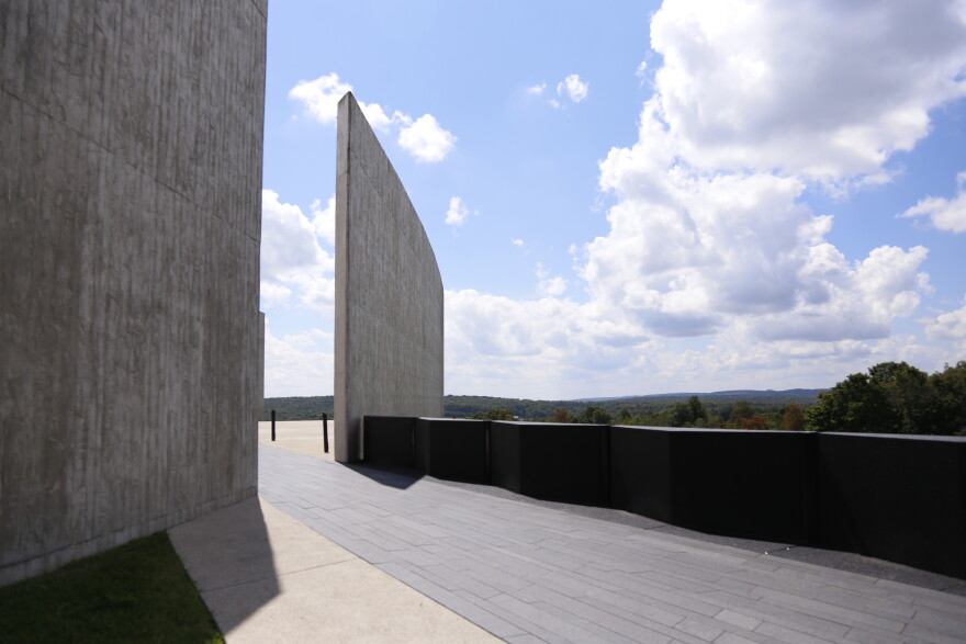A paved walkway runs between tall concrete walls at Flight 93 National Memorial, opening to a broad view of the surrounding hills beneath a partly cloudy sky.