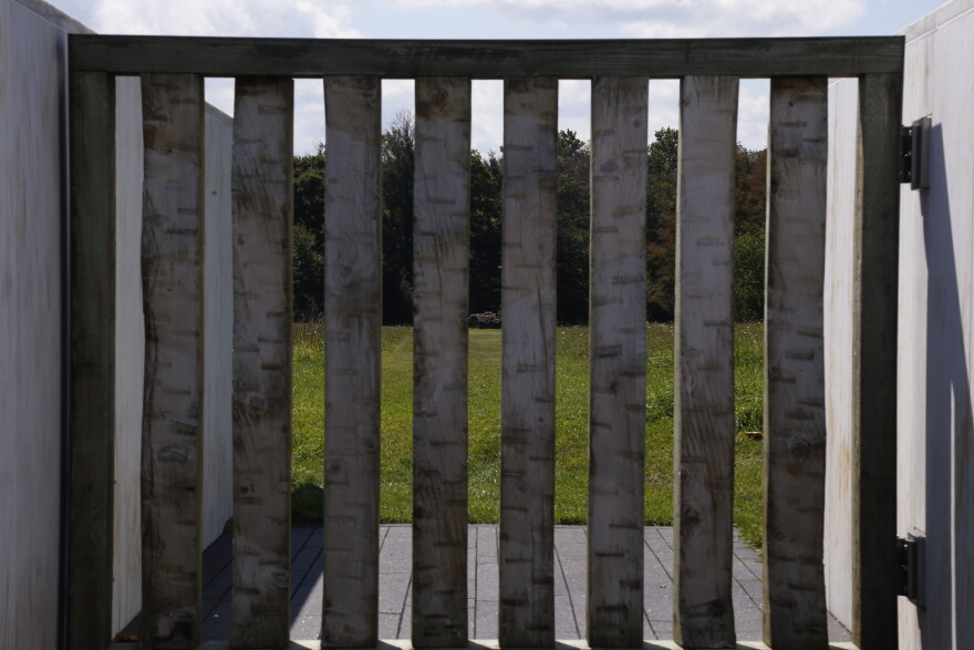 Vertical wooden slats frame a view of a grassy field, with the boulder marking the Flight 93 crash site visible in the distance.