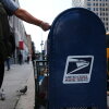A person drops mail into a blue U.S. Postal Service collection box in New York City in 2020.
