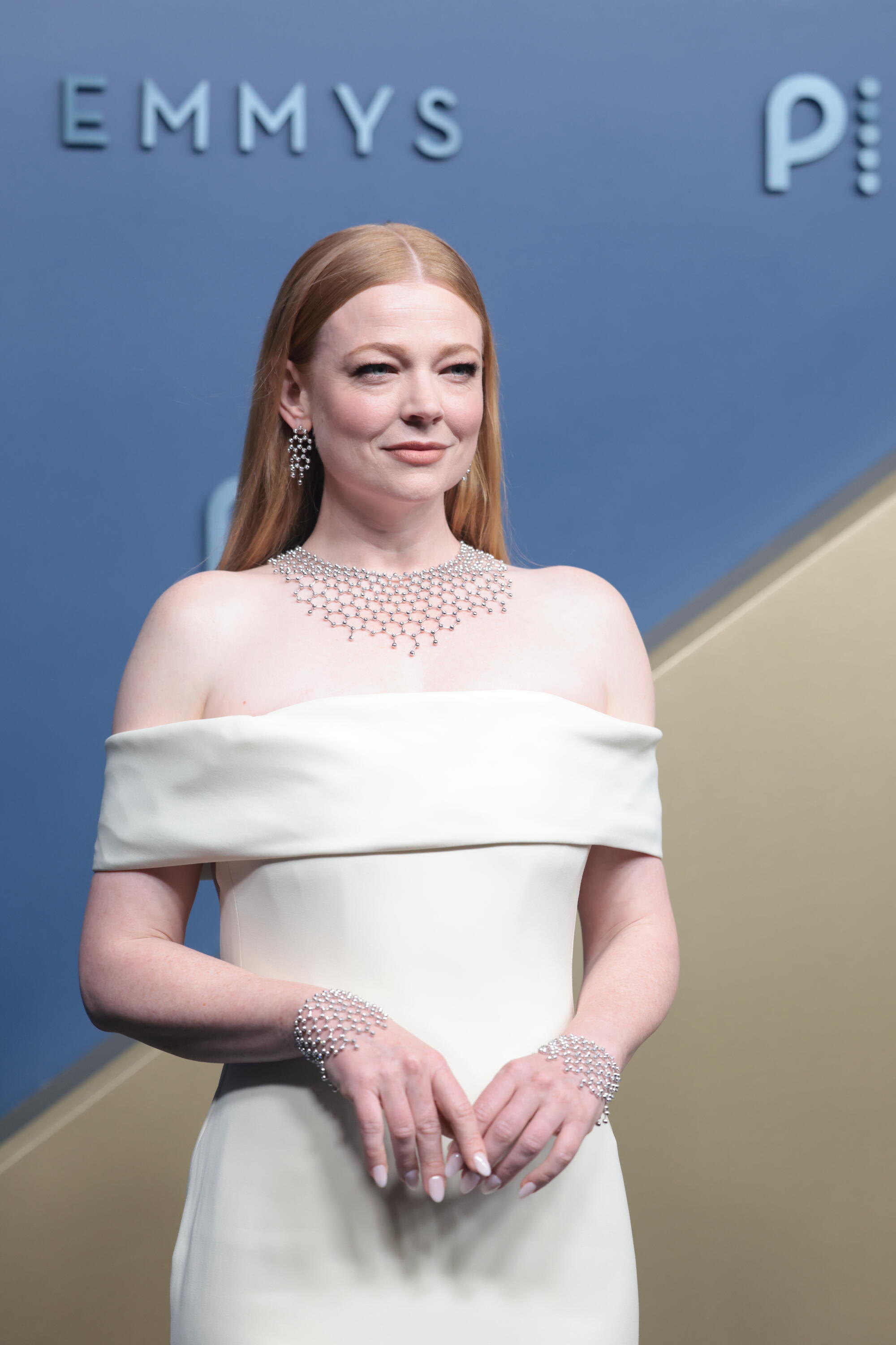 Sarah Snook, wearing a white gown, poses on the Emmys blue carpet. 