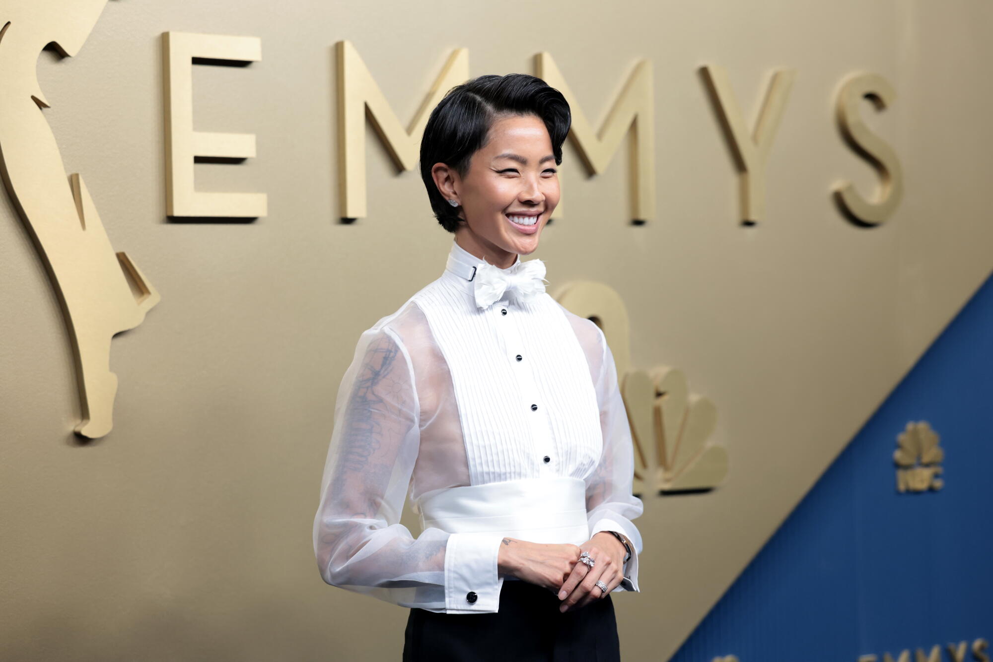 Kristen Kish, wearing a tuxedo shirt, poses on the Emmys blue carpet. 