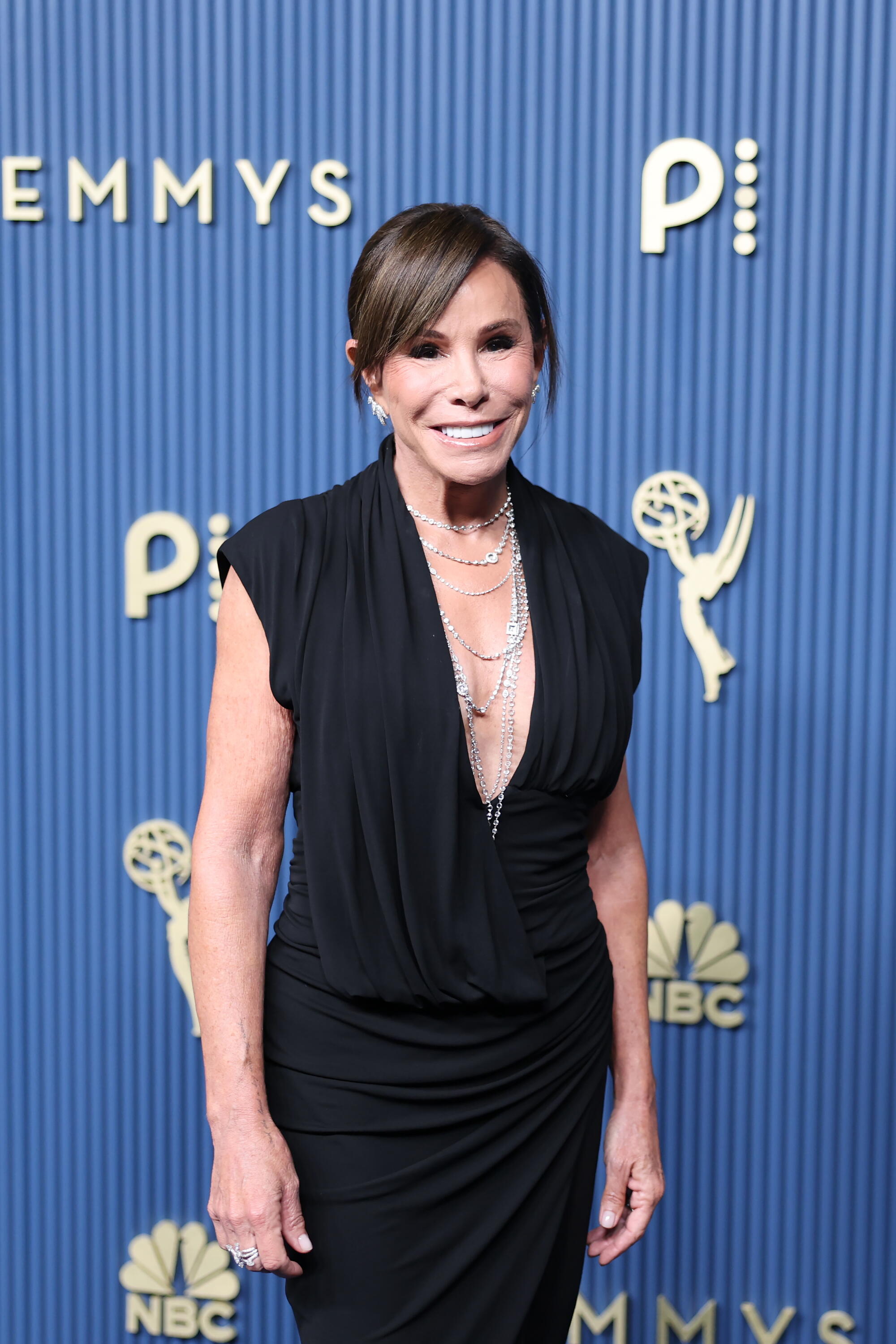 Melissa Rivers, wearing a plunging black dress, poses on the Emmys blue carpet. 