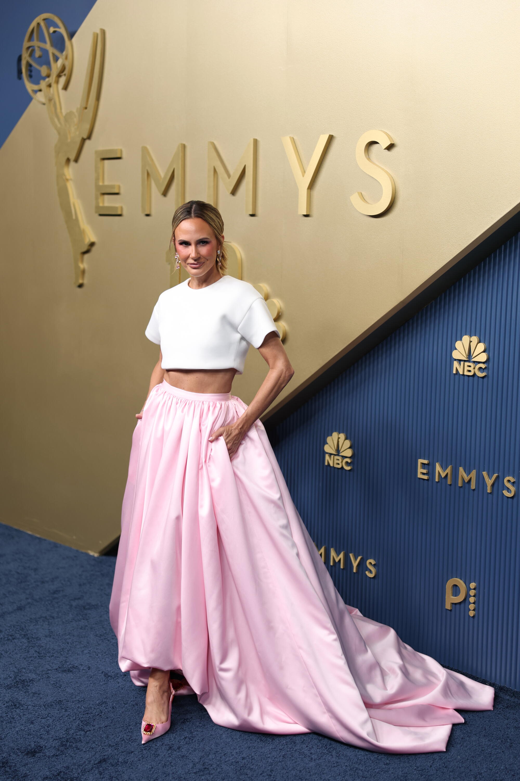 Keltie Knight, wearing a white crop top and pink skirt, poses on the Emmys blue carpet. 