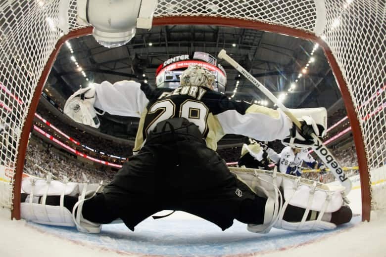 A hockey goaltender framed by the net makes a save during a hockey game.