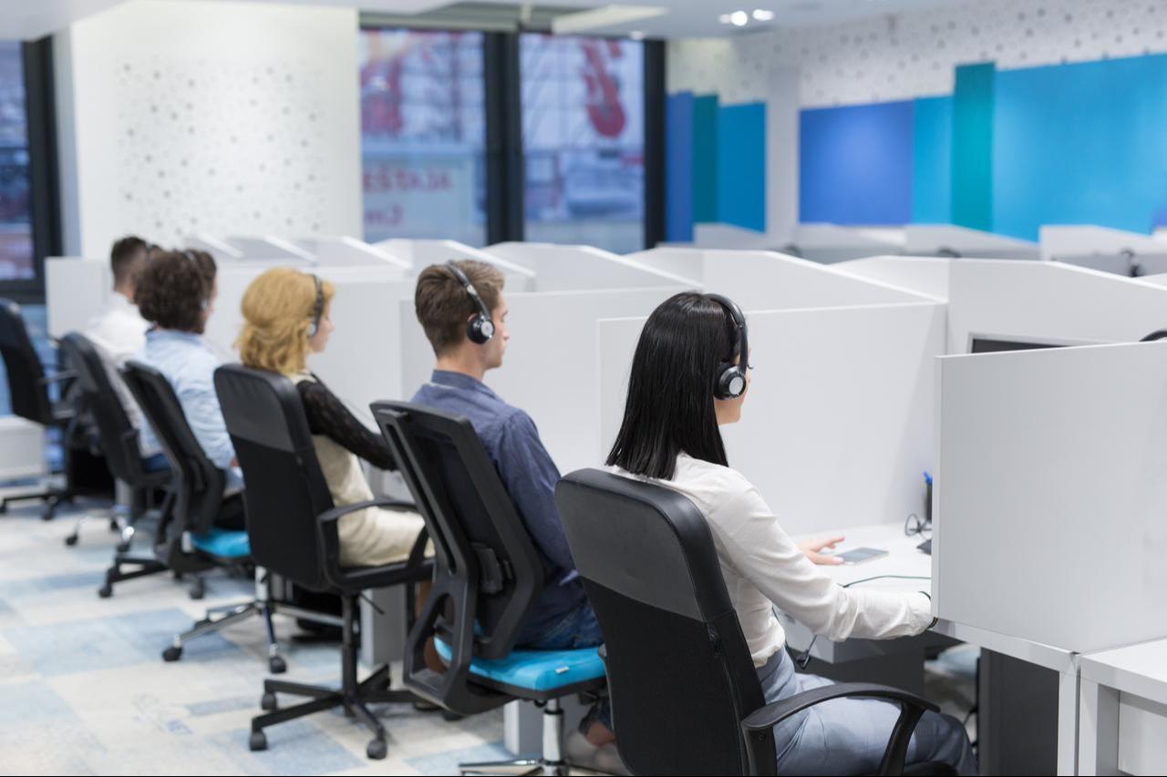 The photo shows a group of young business people with headsets working and giving support to customers in a call center office at an unspecified place and date. (Adobe Stock Photo)