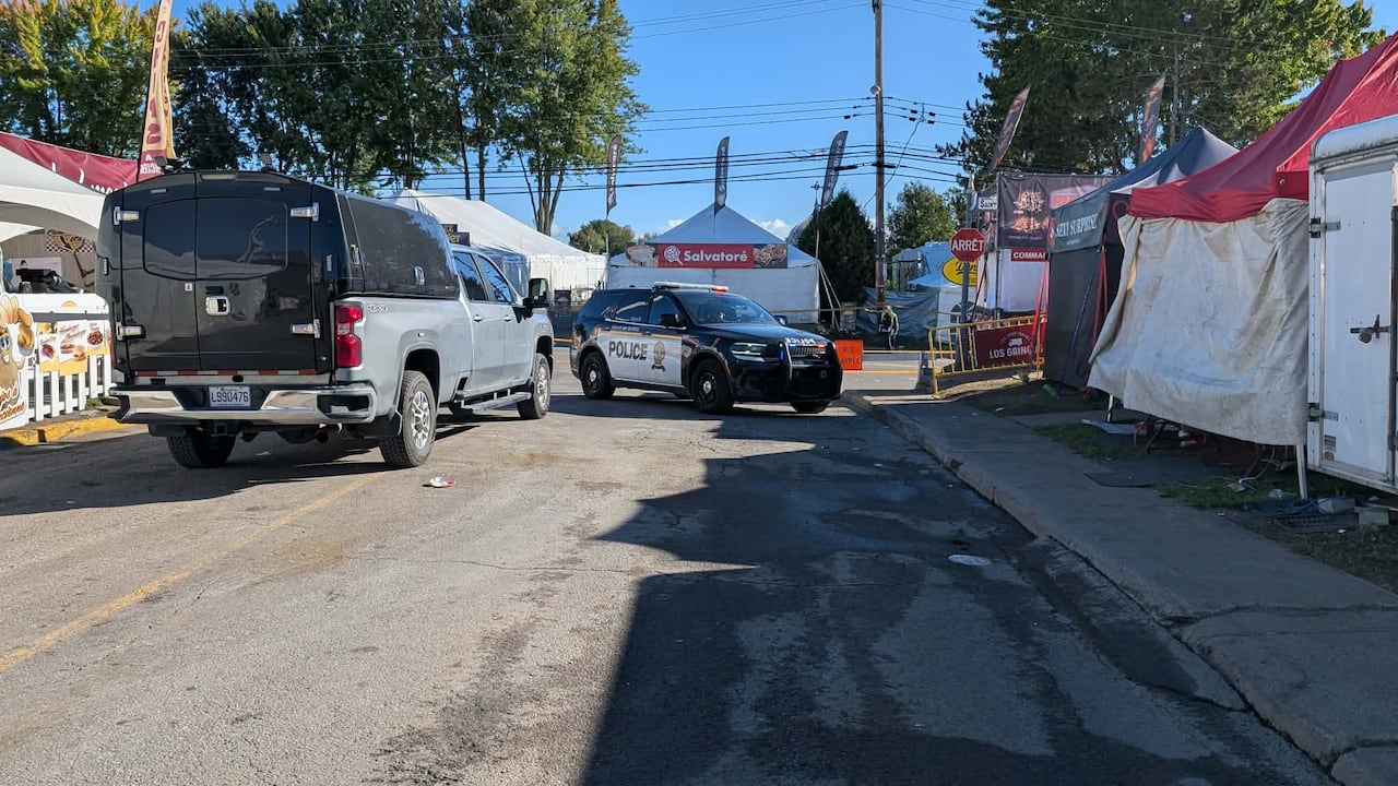 A police SUV and truck are parked in front of police tape in front of festival tents on a road.