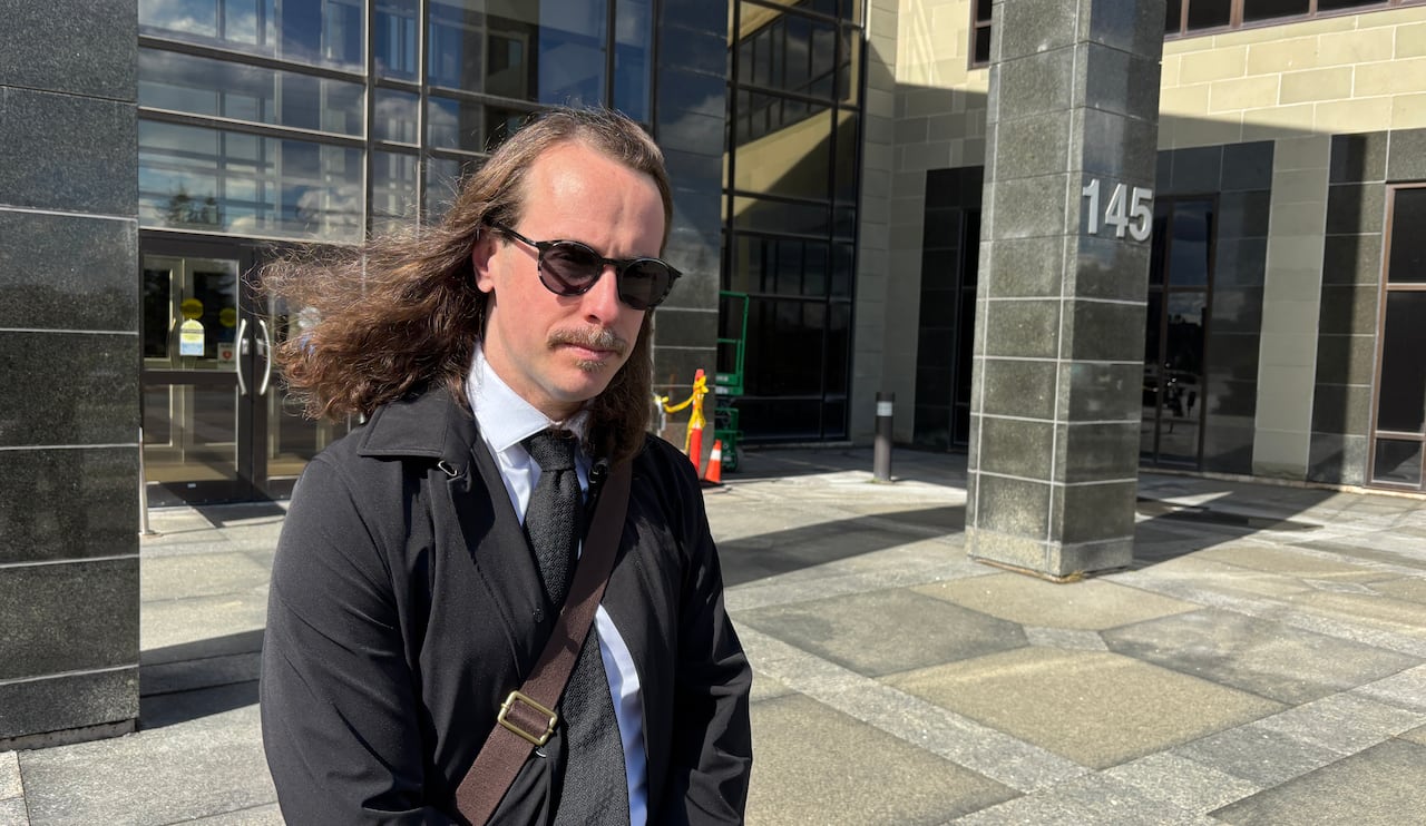 A young man with long hair wearing a suit outside of a courthouse