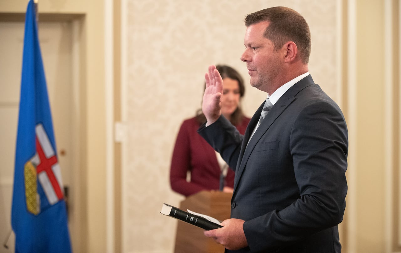 person raises hand as he reads cabinet oath, with political boss behind him.