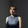 This portrait shows Jo Strogatz photographed from about the waist up. She's wearing a gray sleeveless outfit and a necklace.