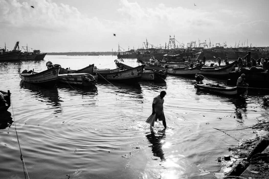 A fisherman wades to the shore from his anchored boat, as the sun rises higher in the sky and the activity on the docks wind down.