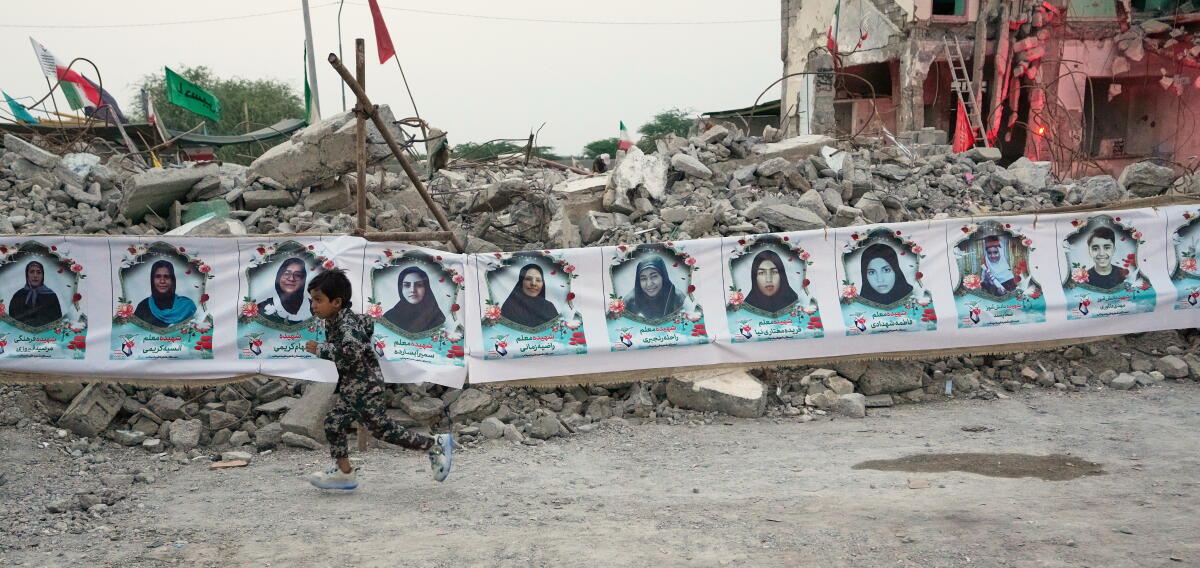 A child runs past a banner strung across the rubble at a school site.