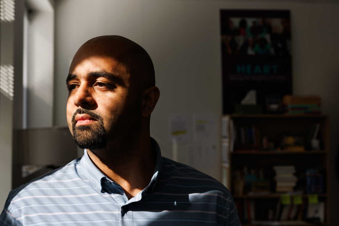 In this photo, Anise Vance is photographed from about the shoulders up in his office. Light is shining on his face, and he's wearing a light-blue collared shirt with light-colored horizontal stripes on it.
