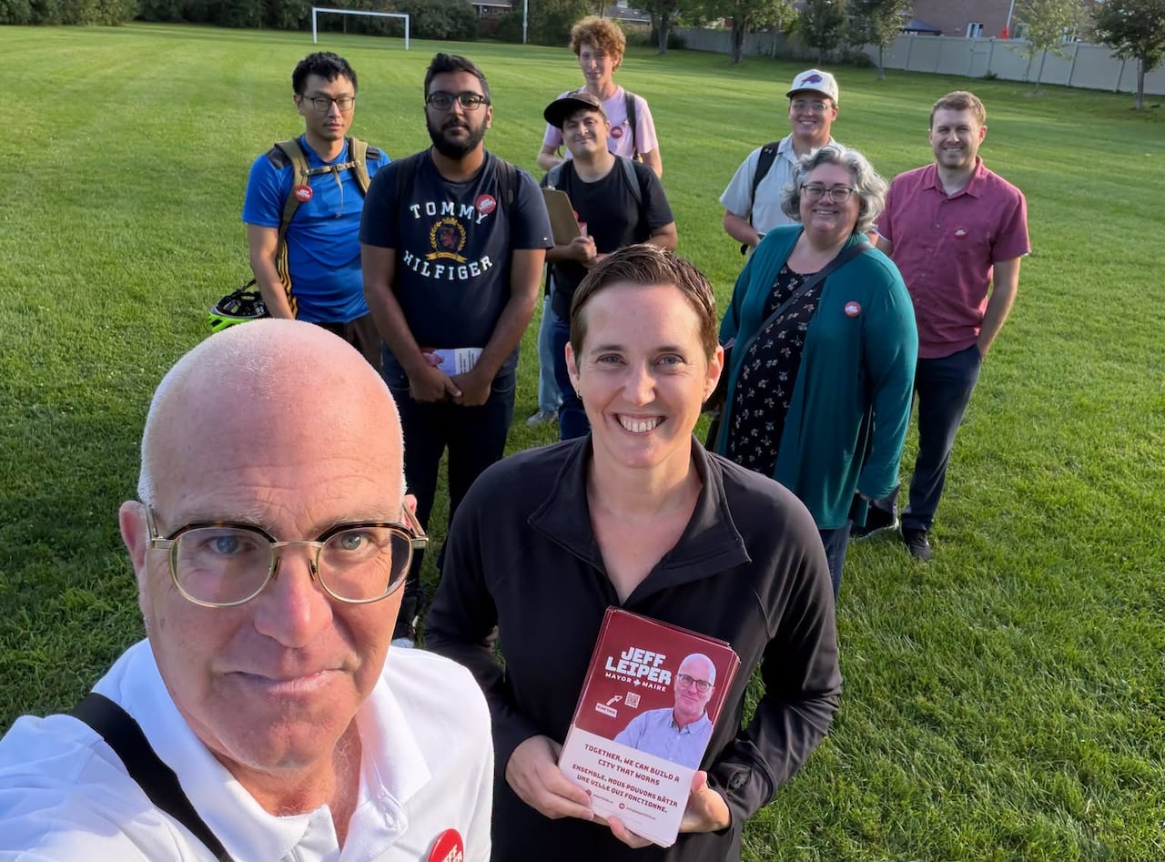 A selfie of a man in a greenspace with a group of people behind him