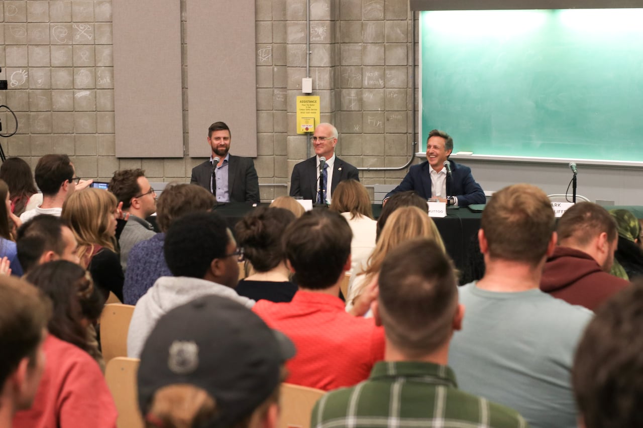 three politicians sit at a table in a university lecture hall
