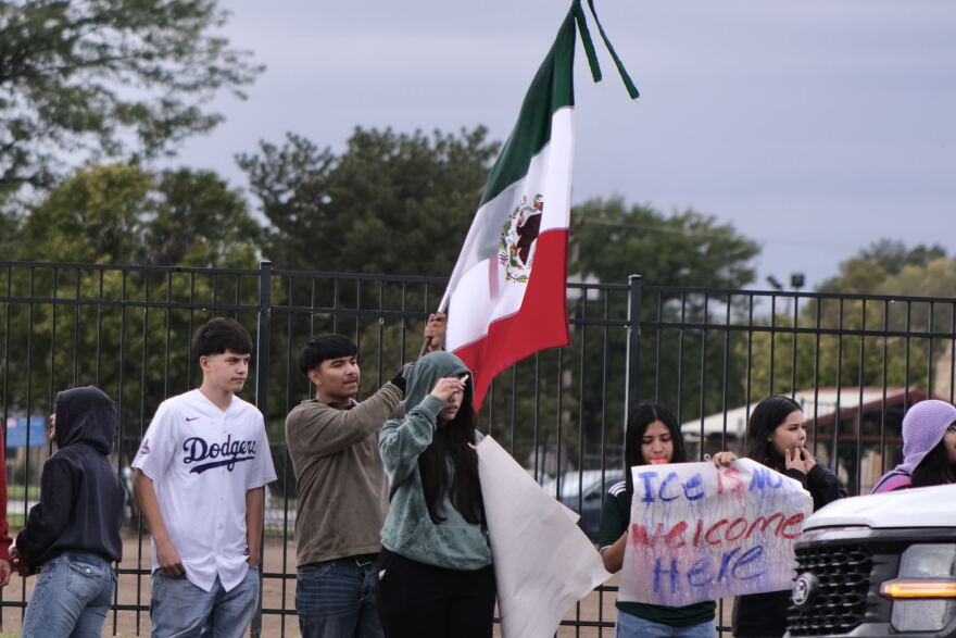 High school students wave wet flags and hold up rain-soaked signs protesting the presence of ICE at in intersection in Liberal, Kansas, on the morning of Sept. 23, 2026.