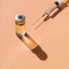 Top view of sterile syringe and unopened vial of liquid remedy placed on orange background
