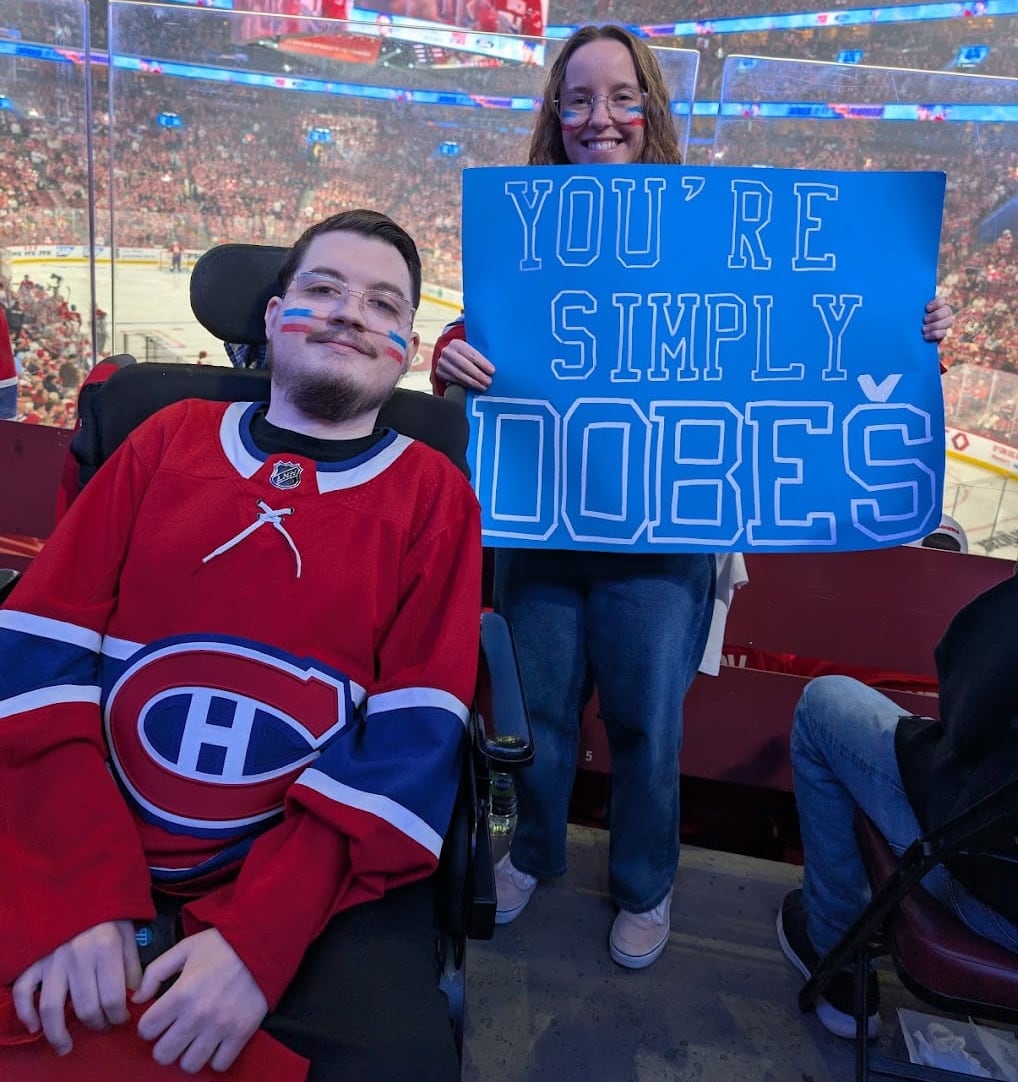 Man in wheelchair with Habs jersey and friend holding a Dobes sign at Bell Centre.