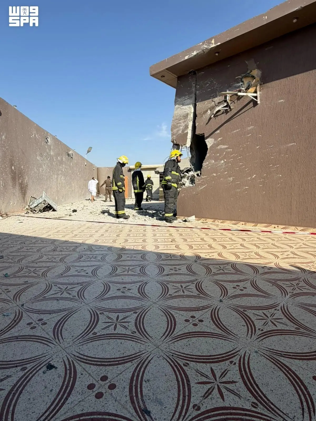 Firefighters inspect significant structural damage to a building, which features a large hole in its wall and scattered debris on the ground following an unspecified incident. (SPA)