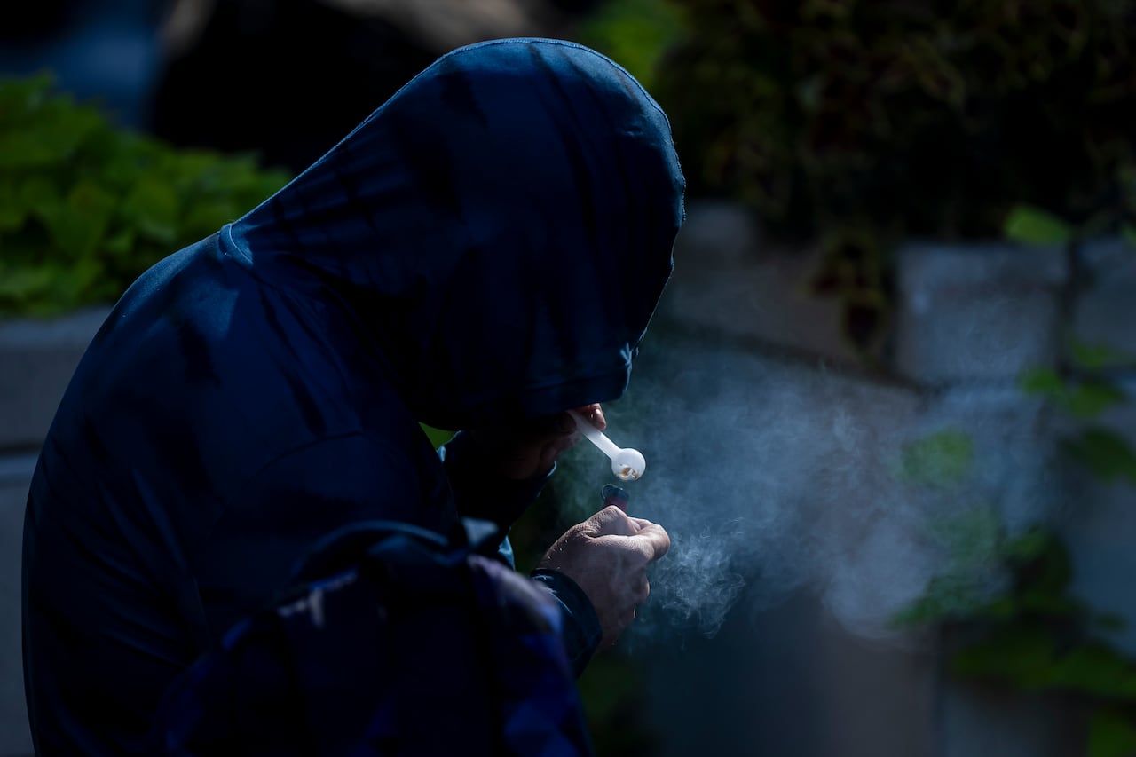 A person in a blue hoodie smokes drugs out of a glass pipe.
