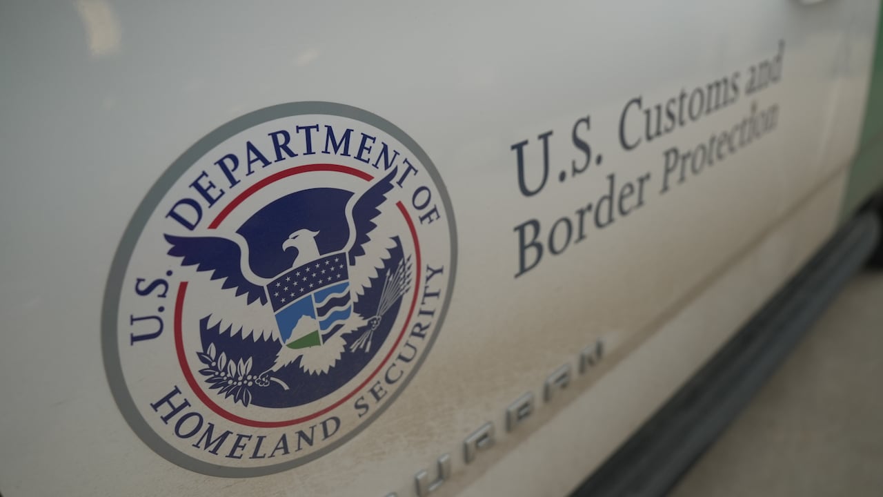 A white vehicle door is shown with the words "U.S. Customs and Border Protection" printed in blue next to the logo for the U.S. Department of Homeland Security.